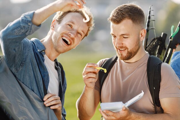 Friends is ready to fishing. Men holding a fishing equipment and looking in a white box with bait for fish. One man wearing rose t-shirt and other blue shirt