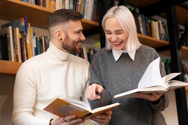 Free Photo friends looking at books in a library and laughing