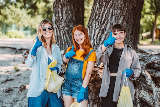 Friends picking up trash from the park. Girls show thumb up.