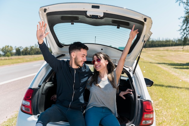 Friends sitting on car trunk making peace sign