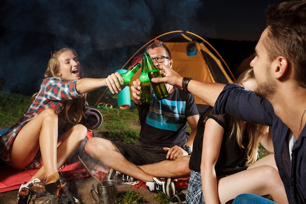 Friends sitting near bonfire, drinking bear, smiling, speaking, resting