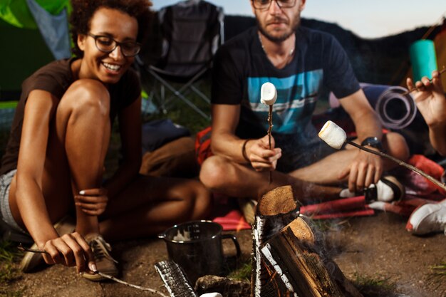 Friends sitting near bonfire, smiling, playing guitar