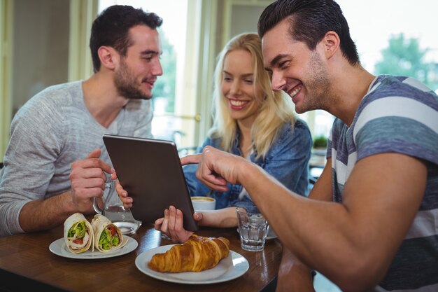 Friends sitting at table and using digital tablet in cafÃ©