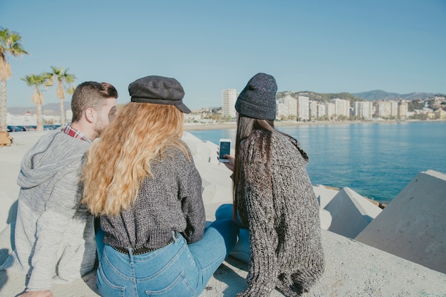 Friends sitting next to water with smartphone