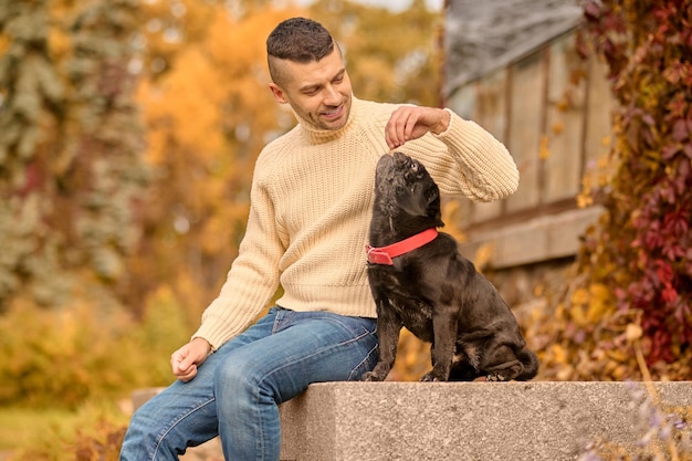 Free Photo friendship. a man in beige turtleneck resting in the park with his pet