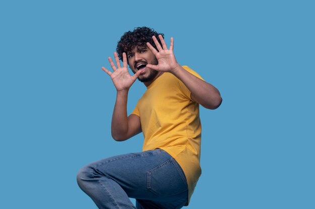 Frightened curly-haired bearded mustached Hindu guy holding two hands with the spread fingers before him