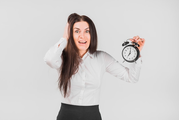 Frightened female holding hair and alarm clock