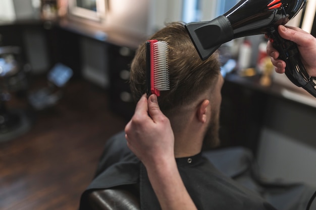 Free photo from above barber combing and drying hair of client