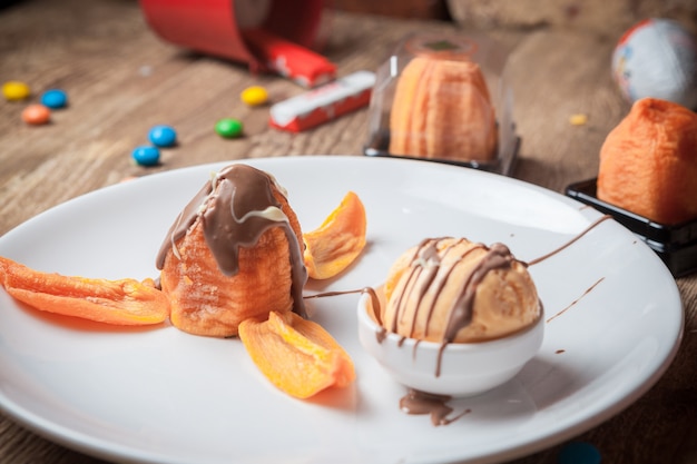 From above ice cream with chocolate syrup and dry apricots in round white plate