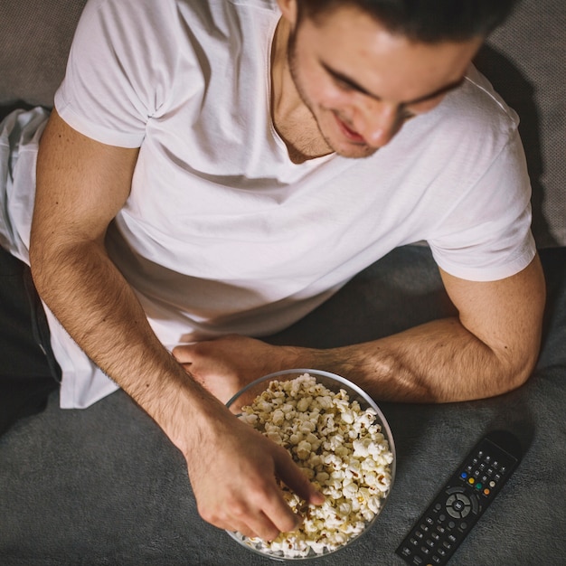 From above man eating popcorn on sofa