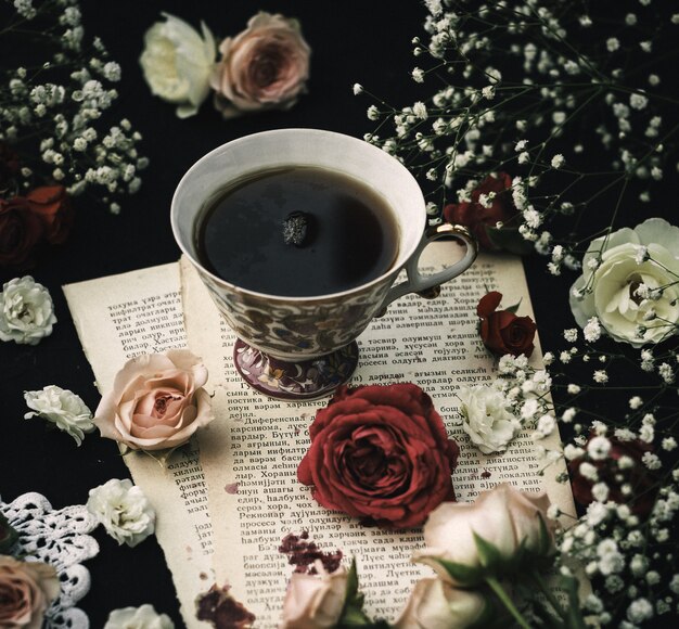 A front close up view hot tea on the paper and around colorful roses on the dark surface