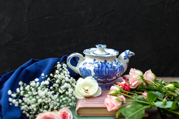 Free photo a front close up view white blue kettle around blue tissue and different colored roses on the dark floor