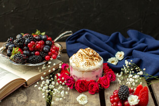 A front close up view yummy dessert around red roses and fresh berries on the brown wooden rustic desk