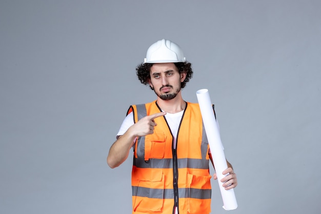 Free photo front close view of angry male construction worker in warning vest with safety helmet and holding blank on gray wall