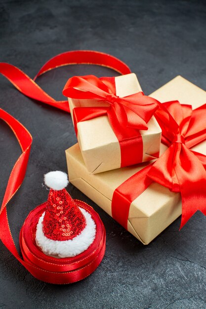 Front close view of beautiful gifts with red ribbon and santa claus hat on a dark table