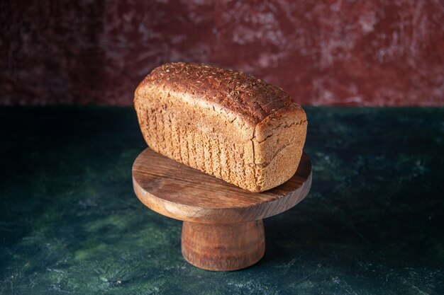 Front close view of black bread slices on wooden board on mixed colors distressed background with free space