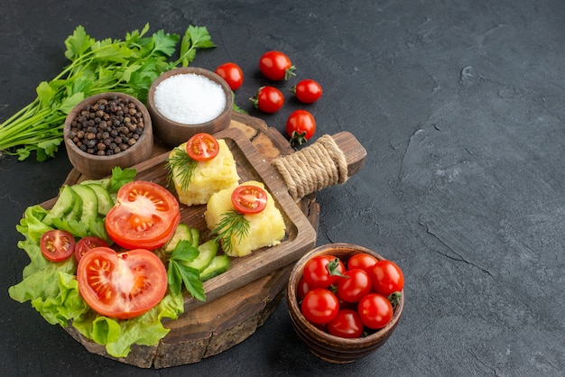 Front close view of chopped fresh vegetables cheese on cutting board and spices green bundle on black surface