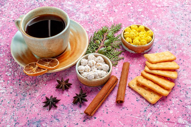 Front close view cup of tea with cinnamon candies and crackers on pink desk