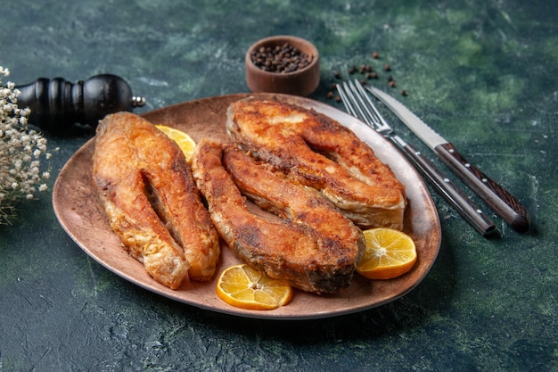 Front close view of delicious fried fishes and lemon slices on a brown plate pepper on mix colors table with free space