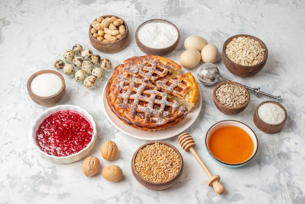 Front close view of delicious jam pie on a white hazelnuts honey eggs flour sugar on ice table