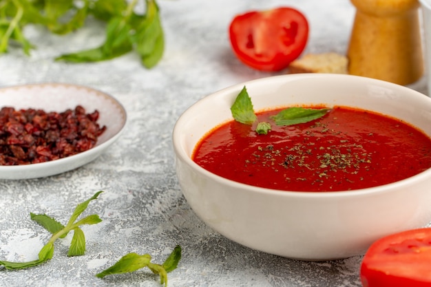 Front close view delicious tomato soup with greens on grey, soup meal dinner vegetable