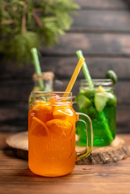 Front close view of detox water and fresh juice in bottles with tubes on brown wooden background