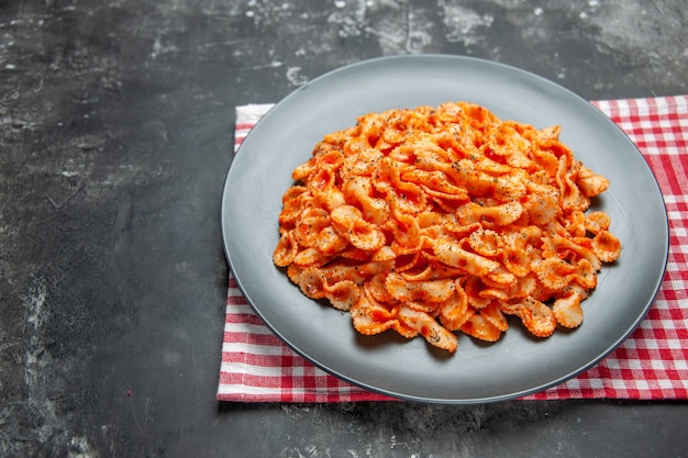 Free photo front close view of easy pasta meal for dinner on a black plate on a red stripped towel