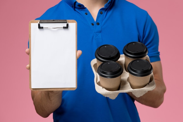 Free Photo front close view male courier in blue uniform holding delivery coffee cups and notepad on the pink, uniform service job delivery