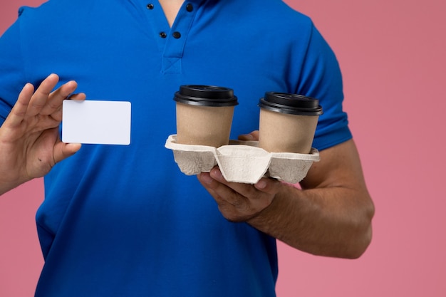 Free photo front close view male courier in blue uniform holding delivery coffee cups and white card on pink, uniform service delivery