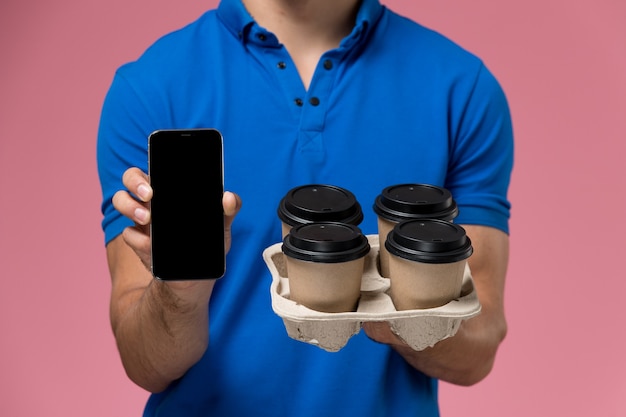 Free Photo front close view male courier in blue uniform holding phone and coffee cups on pink, worker uniform service delivery