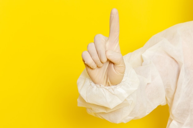 Front close view of male scientific worker in special protective suit raising his finger on the yellow wall