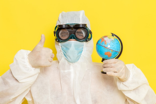 Free photo front close view male scientific worker in special suit holding little round globe on the yellow desk