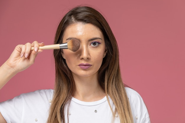 Free photo front close view young female in white shirt holding make-up brush on pink, model woman pose girl beauty