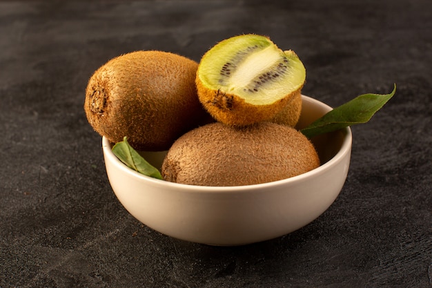 Free photo a front closed up view brown kiwis fresh ripe isolated juicy mellow and whole fruits along with green leaves inside white plate