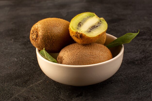 A front closed up view brown kiwis fresh ripe isolated juicy mellow and whole fruits along with green leaves inside white plate