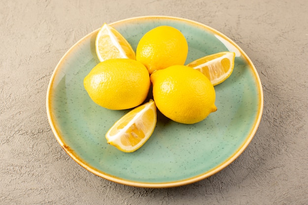 Free photo a front closed up view yellow fresh lemons ripe mellow and juicy whole and sliced inside green plate on the grey