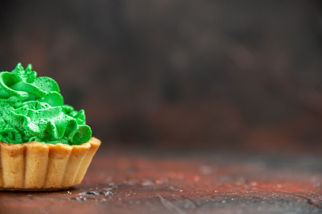 Front half view small tart with green pastry cream on dark red table with copy space