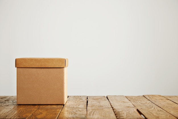 Front shot of an unlabeled square beige cardboard box with cover on wooden floor isolated on white