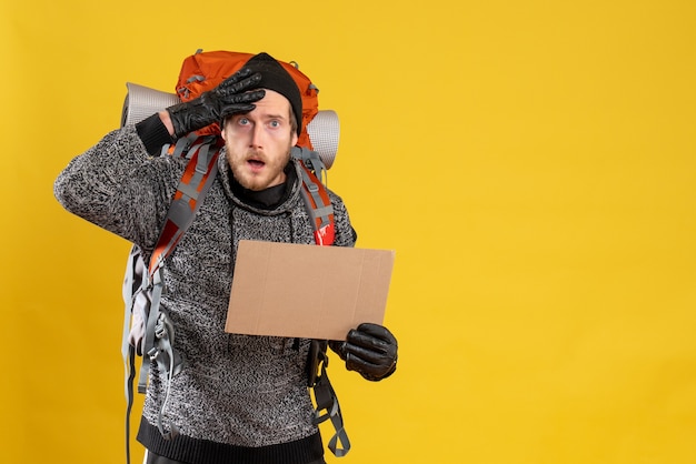 Front view of agitated male hitchhiker with leather gloves and backpack holding blank cardboard