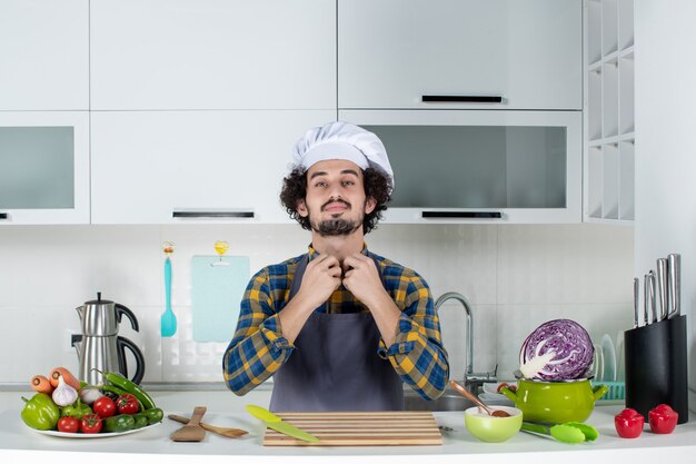 Front view of ambitious male chef with fresh vegetables and cooking with kitchen tools and in the white kitchen