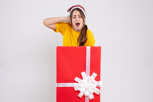 Free photo front view angry girl with santa hat holding her head standing behind big xmas gift