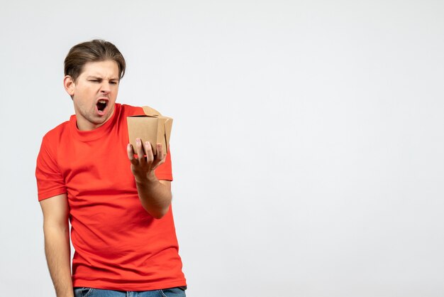 Front view of angry nervous young guy in red blouse holding small box on white background