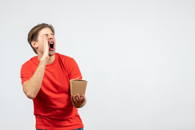 Front view of angry young guy in red blouse holding small box and calling someone on white background