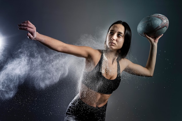 Free photo front view of athletic female rugby player holding ball with dust