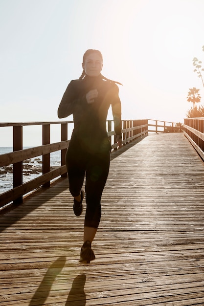 Free photo front view of athletic woman jogging by the beach with copy space