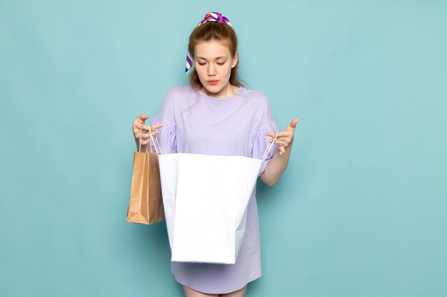 A front view attractive female in blue shirt-dress holding shopping packages on blue