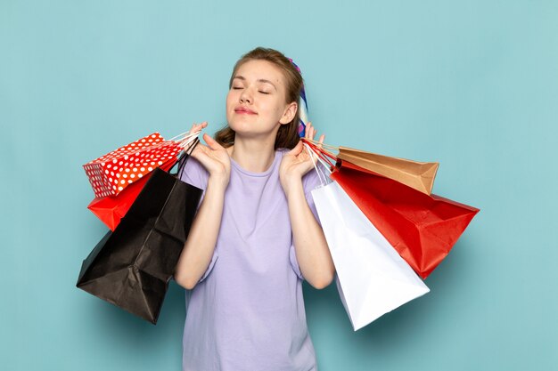 A front view attractive female in blue shirt-dress holding shopping packages on blue