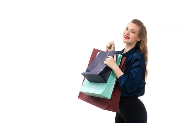 A front view attractive young lady in blue blouse black trousers posing holding shopping packages smiling happy on the white background fashion elegant clothing