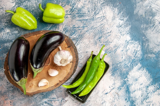 Front view aubergines garlic on tree wood board peppers hot green peppers on black plate on blue-white background free space