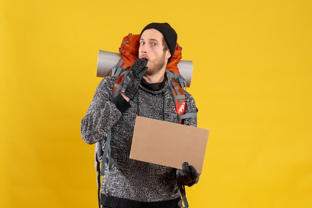 Front view of baffled male hitchhiker with leather gloves and backpack holding blank cardboard